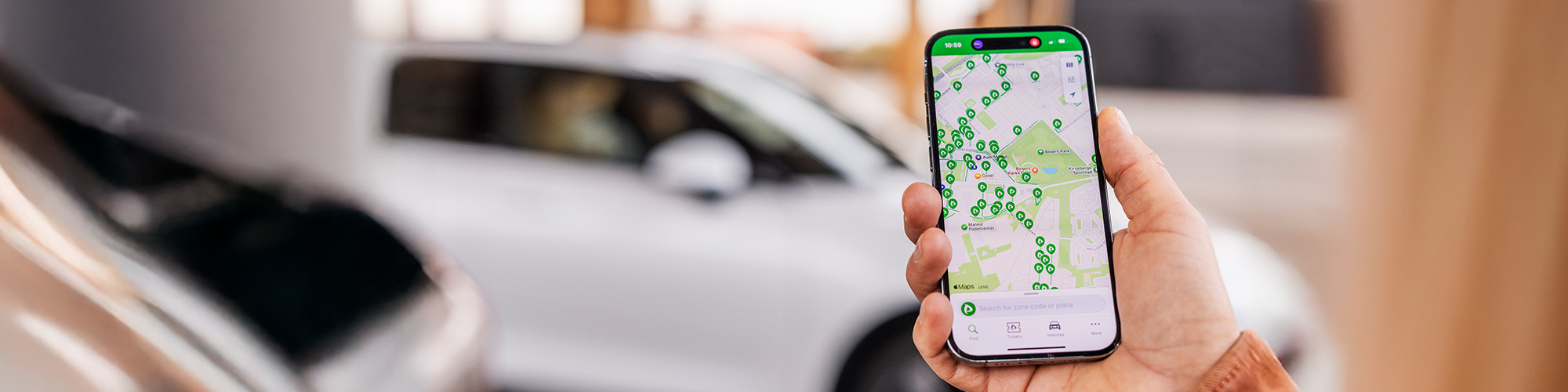 Hand hält ein Smartphone das eine Karte auf dem Display zeigt, im Hintergrund ist ein Auto zu sehen