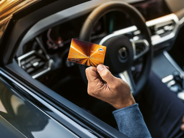 Bildausschnitt von einem Auto, eine Person hält den Arm hoch und eine Karte in der Hand