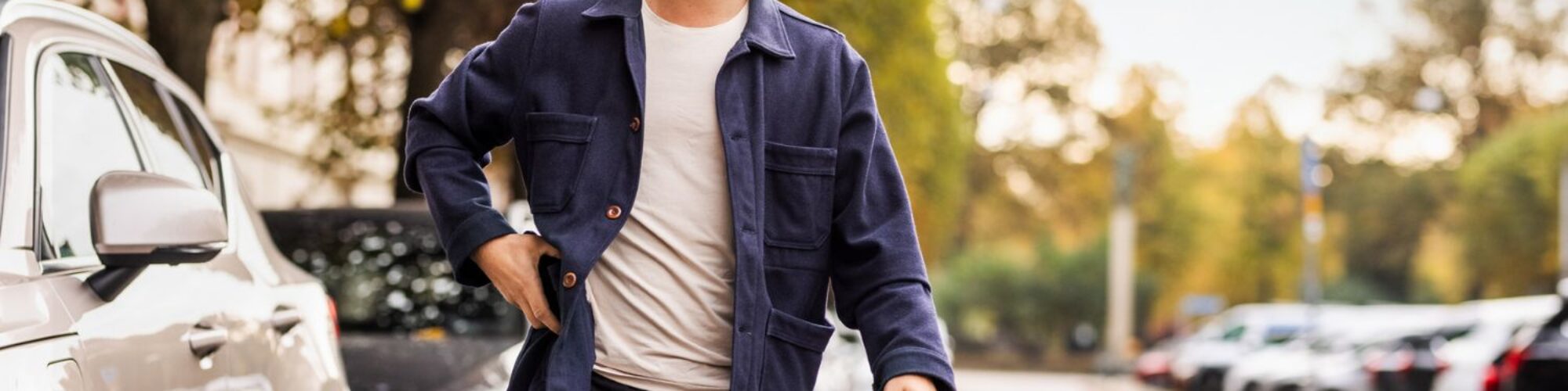 Mann mit Kinnlangen Haaren und Schnauzbart geht auf der Straße, parkende Autos im Hintergrund