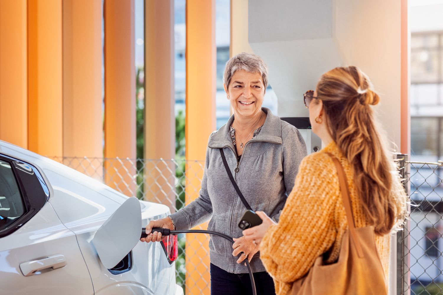 Två kvinnor ser på varandra medans den ena laddar sin elbil