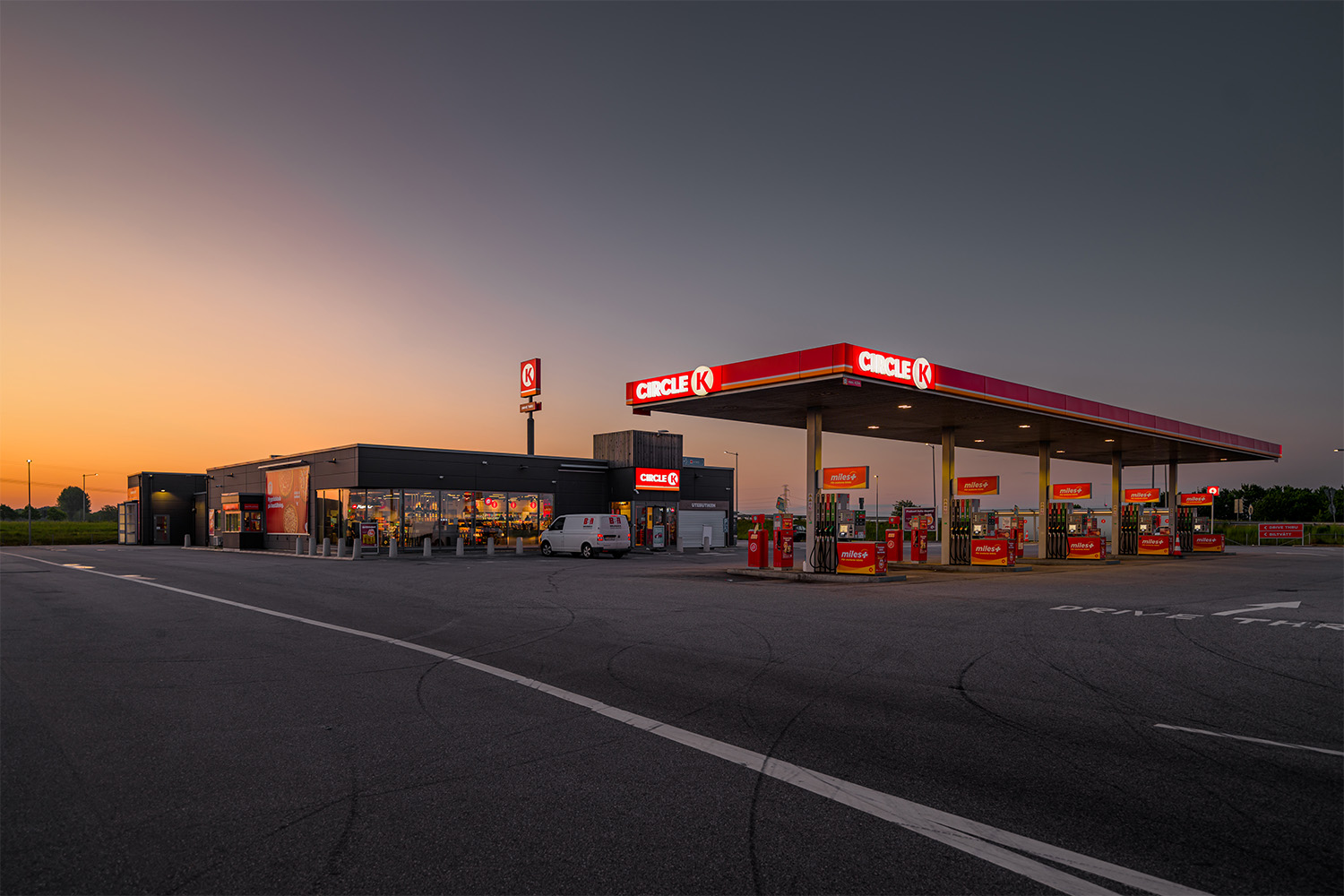 Bensinstation från Circle K i solnedgång, med upplysta pumpar och butik i bakgrunden.