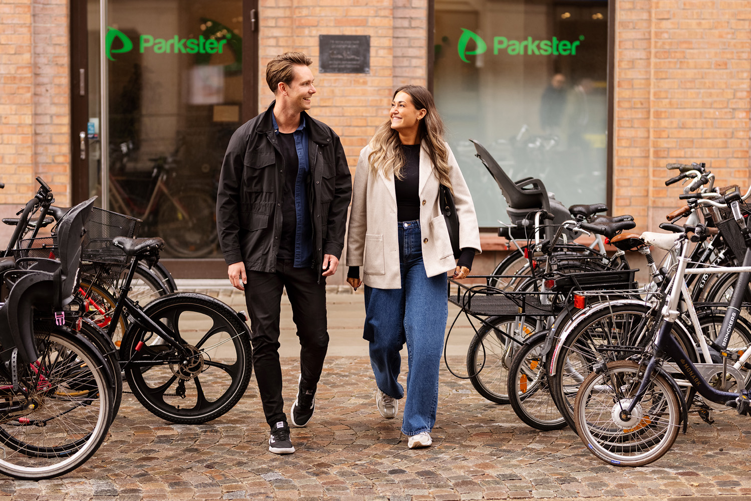 En man och en kvinna går utanför Parksters kontor i Lund. Tittar på varandra och ler. Cyklar står på båda sidorna.
