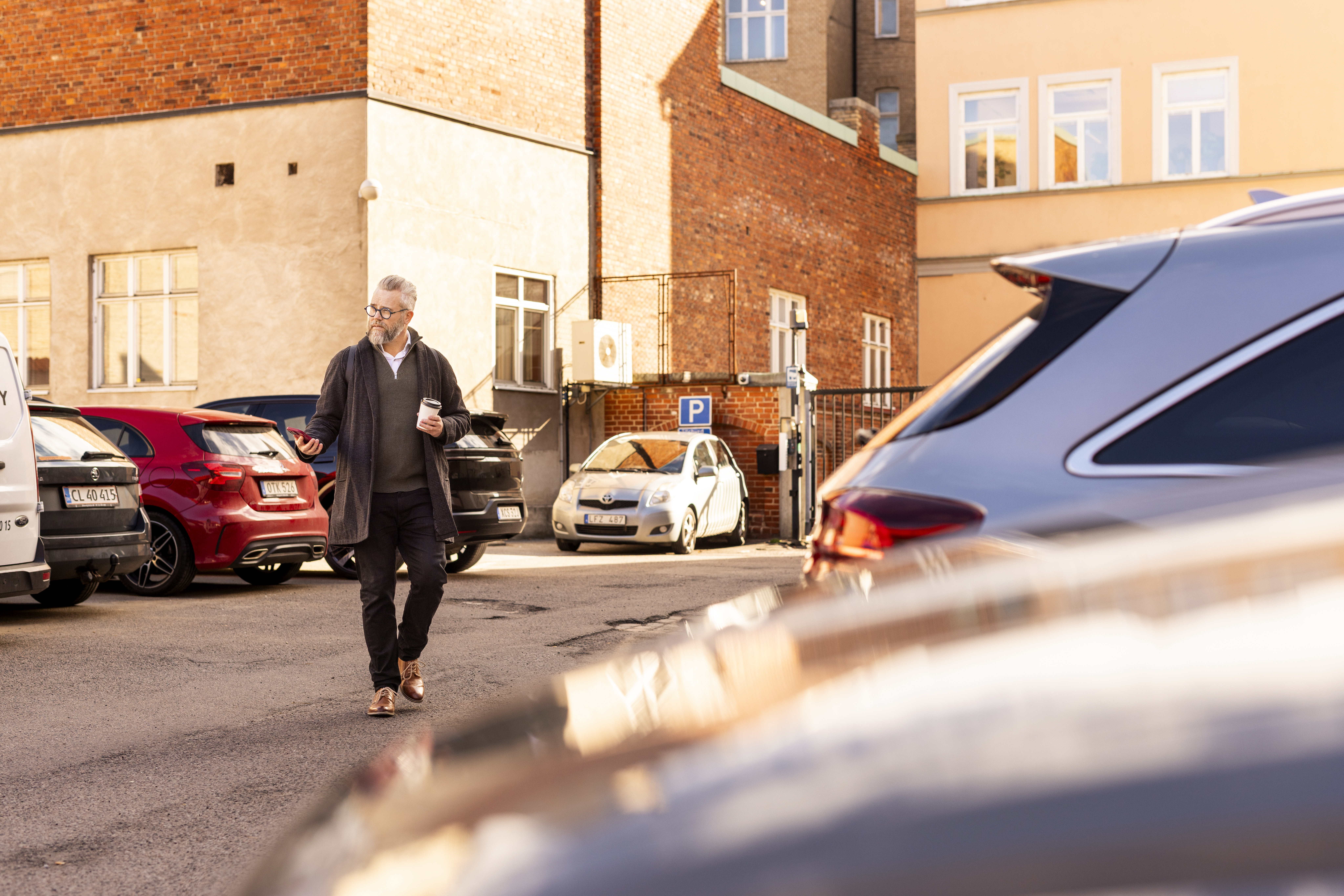 A business man walking towards a car with a phone in his hand