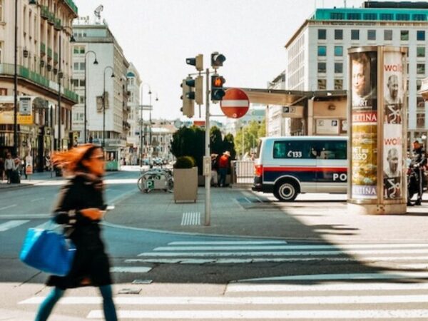 en bild på stadsbruset i Vienna, kvinna går över övergångställe och parkerade bilar.