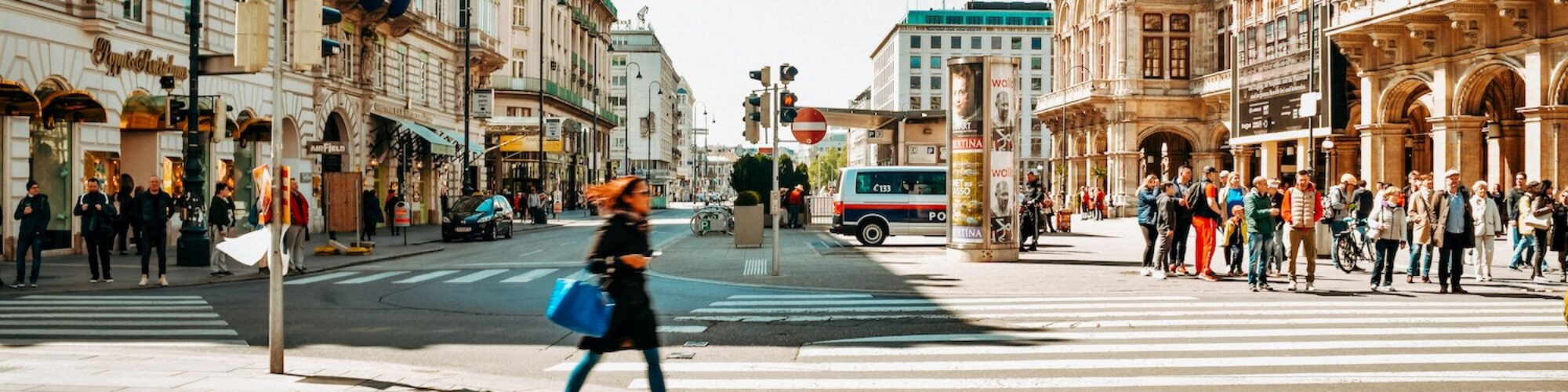 en bild på stadsbruset i Vienna, kvinna går över övergångställe och parkerade bilar.